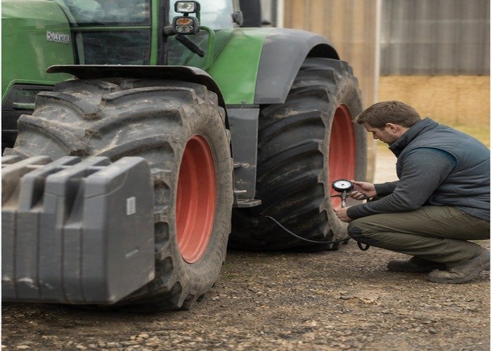Operator checking tractor tire pressure and front ballast on a stopped machine