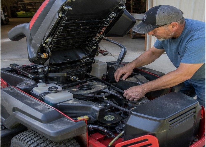 Owner inspecting belts cooling fans and linkages on a stopped cooled zero turn mower Owner inspecting belts cooling fans and linkages on a stopped cooled zero turn mower