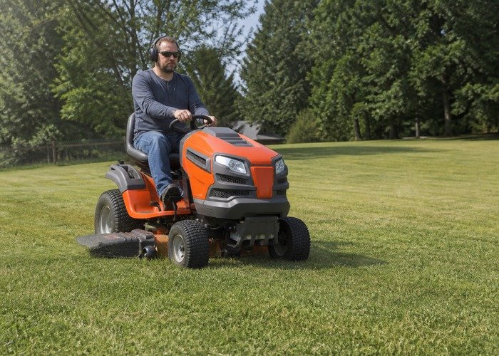 Operator safely mowing an open large yard with a riding lawn tractor