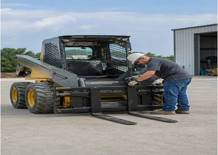 Operator inspecting grounded pallet forks and coupler locks Operator inspecting grounded pallet forks and coupler locks