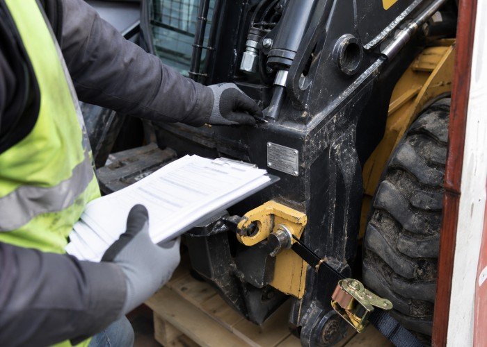 Inspector checking skid steer tie-down and serial details