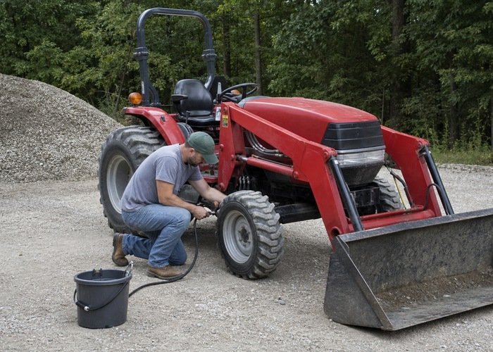 Operator checking tractor front tire pressure after loader work