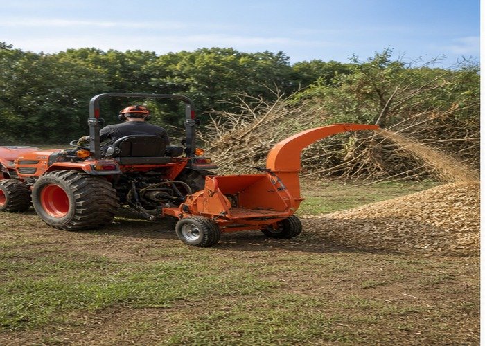 Compact tractor operating a PTO wood chipper at a brush cleanup site