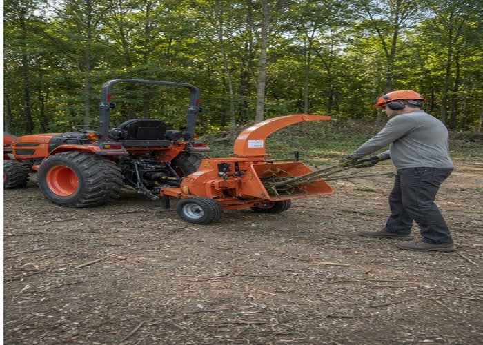 Operator feeding straight branches from the side of a tractor wood chipper Operator feeding straight branches from the side of a tractor wood chipper