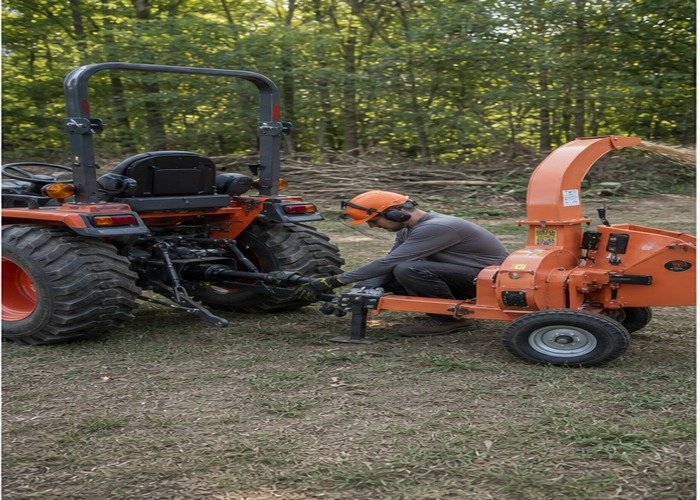 Operator inspecting the stopped tractor wood chipper hitch and PTO shield Operator inspecting the stopped tractor wood chipper hitch and PTO shield