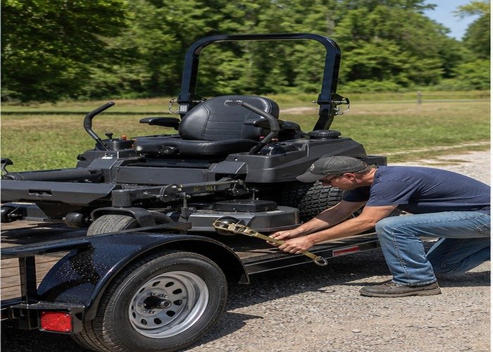 Operator attaching a tie-down to a mower frame point Operator attaching a tie-down to a mower frame point
