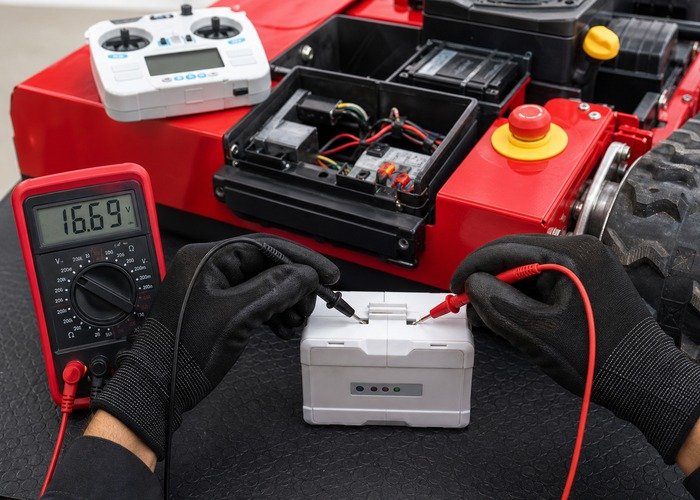 Technician testing a remote mower controller battery beside the emergency stop and receiver compartment