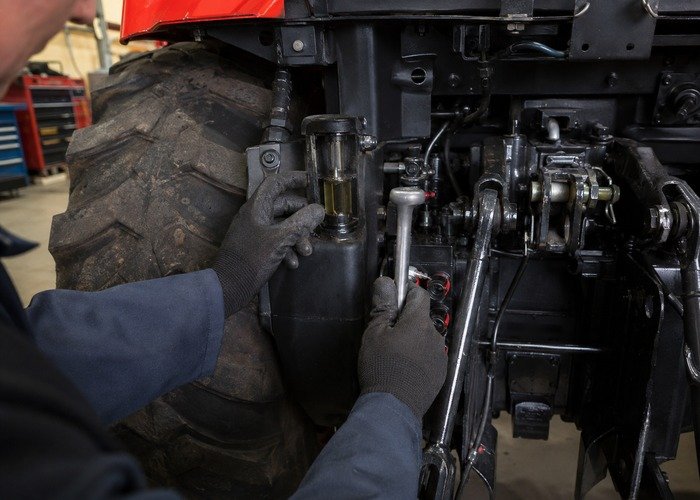 Technician inspecting tractor hydraulic oil level and position-control linkage