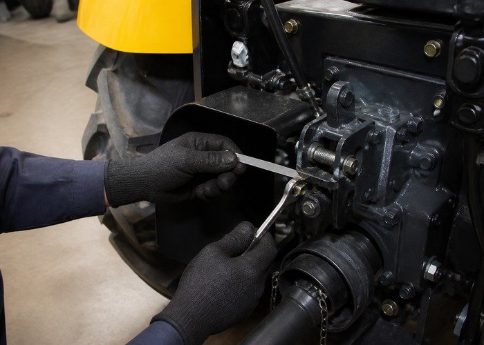 Technician checking tractor PTO clutch adjustment with a feeler gauge and wrench