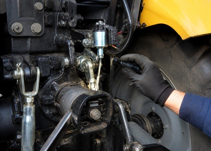 Technician inspecting tractor PTO solenoid and engagement linkage near the rear housing