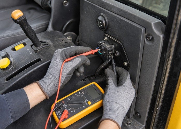 Technician testing a compact tractor PTO switch connector with a multimeter
