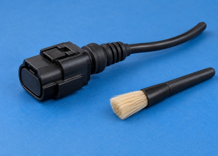 Illustrative single closed dry electrical connector with intact cable and boot beside unused soft brush