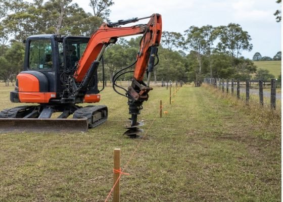 Mini excavator with auger aligned beside a marked fence line