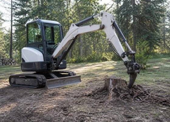 Mini excavator using a ripper beside a tree stump