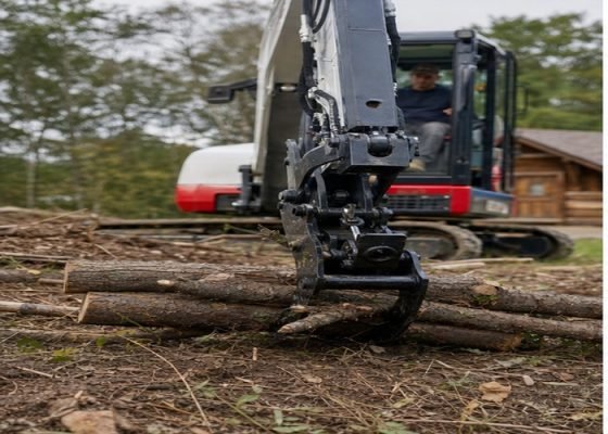 Mini excavator hydraulic thumb gripping small logs low to the ground during rural cleanup