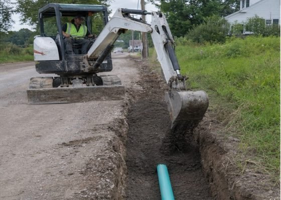 Mini excavator placing suitable backfill into a utility trench in shallow lifts