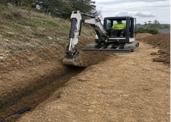 Mini excavator digging from a firm level working platform beside a trench