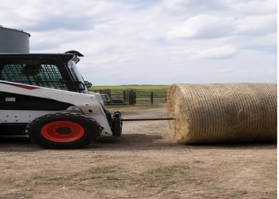 Skid steer aligning a bale spear with the center of a round bale