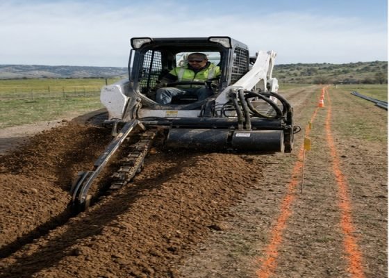 Skid steer chain trencher cutting a marked irrigation trench through rural soil