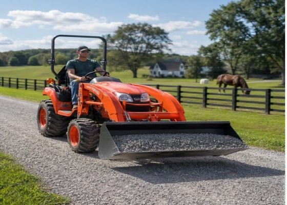Compact tractor with front loader moving gravel on a rural property lane