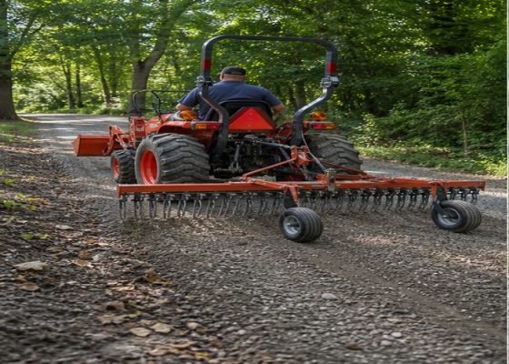 Compact tractor using a rear landscape rake to recover loose gravel on a rural lane