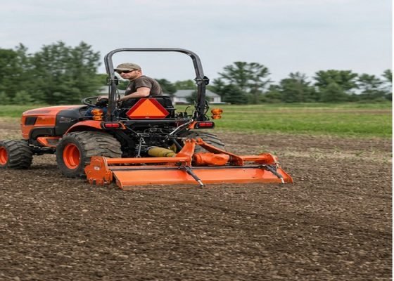Compact tractor operating a rotary tiller with a guarded PTO driveline
